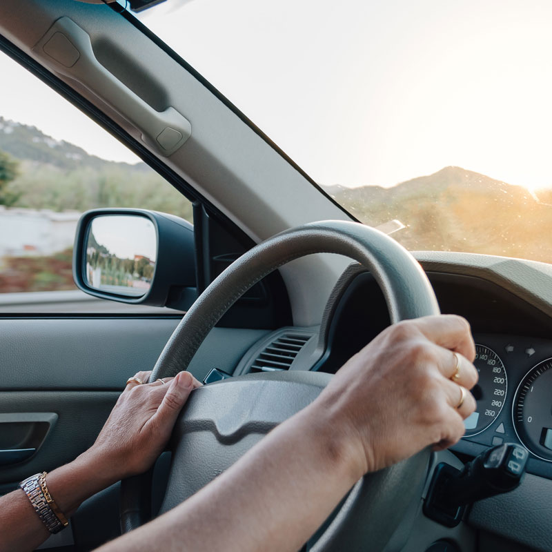 hands of woman driving a car at sunset